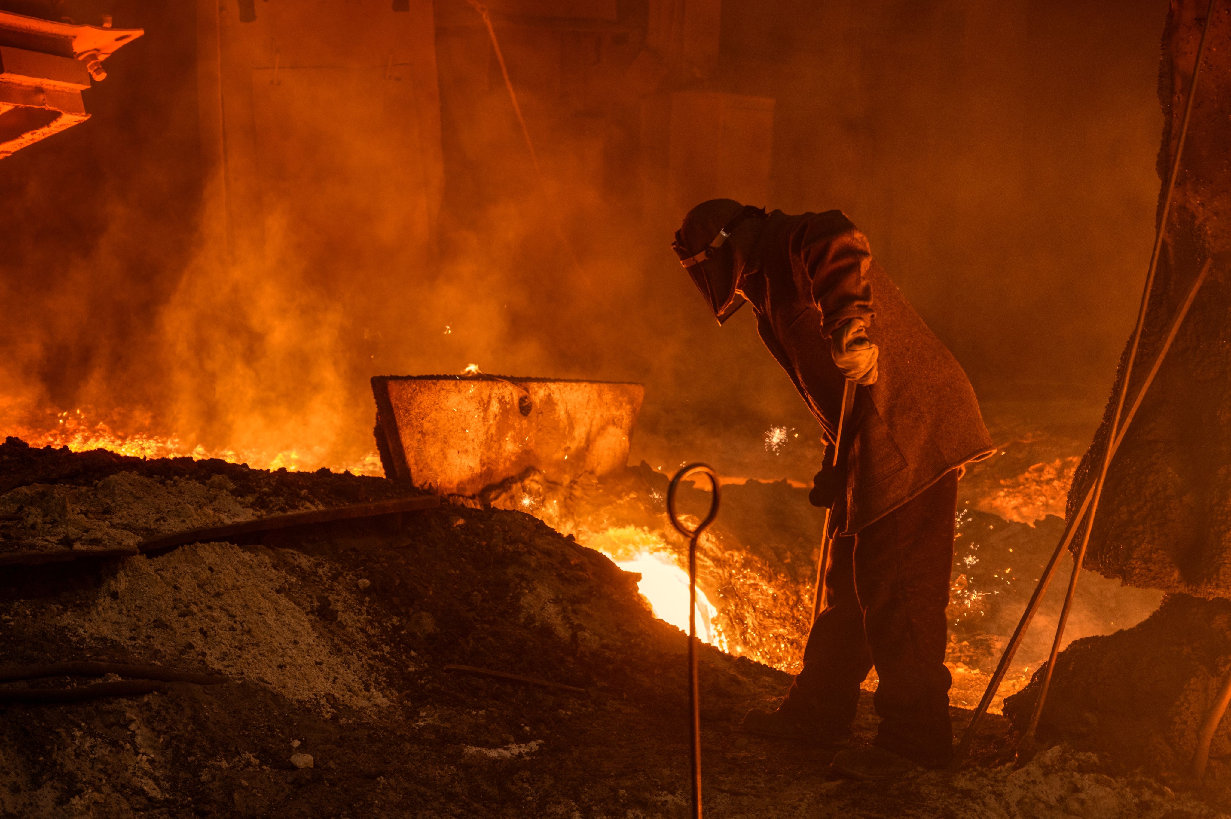 A man works with molten metal during the process of releasing pig iron from a blast furnace. 